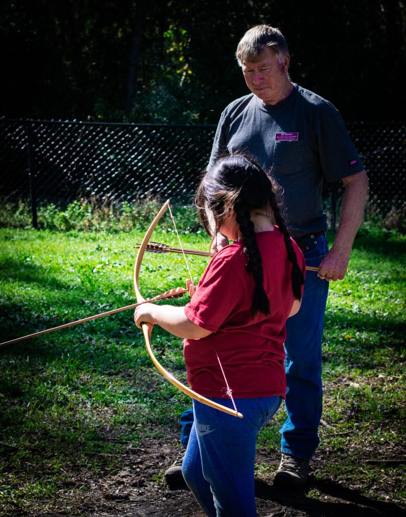 Bill Skinner instructs a child how to use a bow and arrow